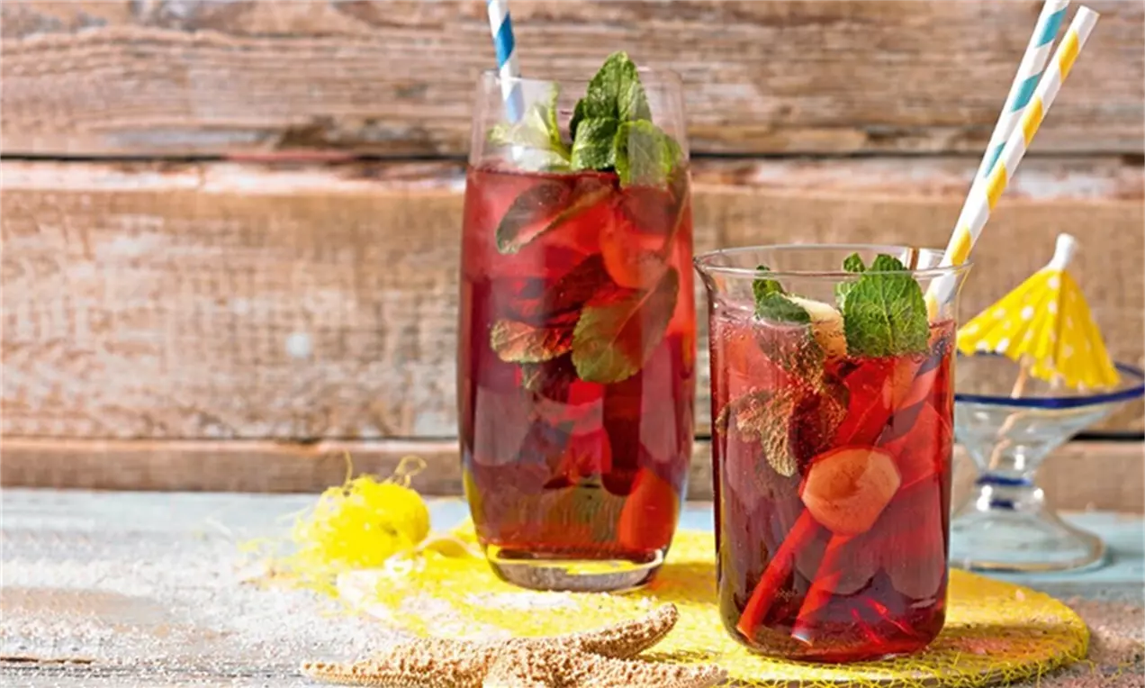 Skaidriuose stiklinėse sodriai raudonas vyšnių limonadas su imbiero griežinėliais, žalumynų lapeliais ir spalvotais dryžuotais šiaudeliais